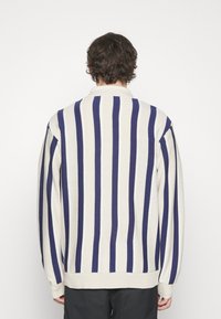 Cremefarbener Pullover mit auffälligen, navyblauen vertikalen Streifen, mit Kragen, langen Ärmeln und geripptem Saum. Weiches, strukturiertes Strickmaterial.