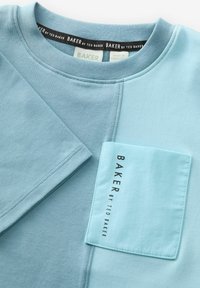 Světle modrá mikina s kulatým výstřihem, má přední kapsu v tmavší modré barvě a logo "BAKER by TED BAKER" na kapse.