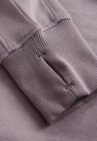 Sweat-shirt violet clair en matière douce avec des poignets côtelés. Dispose d'un trou pour le pouce au niveau du poignet et d'une texture lisse. Design simple sans motifs.