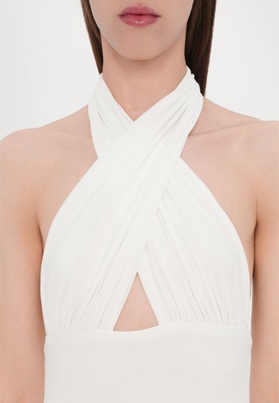Top blanco de cuello halter con diseño de tela entrelazada, que presenta un corte en forma de ojal en el centro y un material suave y elástico.