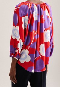 Rote Bluse mit floralen Mustern in Lila und Weiß, gerafftem Ausschnitt, 3/4-Ärmeln mit elastischen Bündchen, weichem Stoff und entspanntem Schnitt.