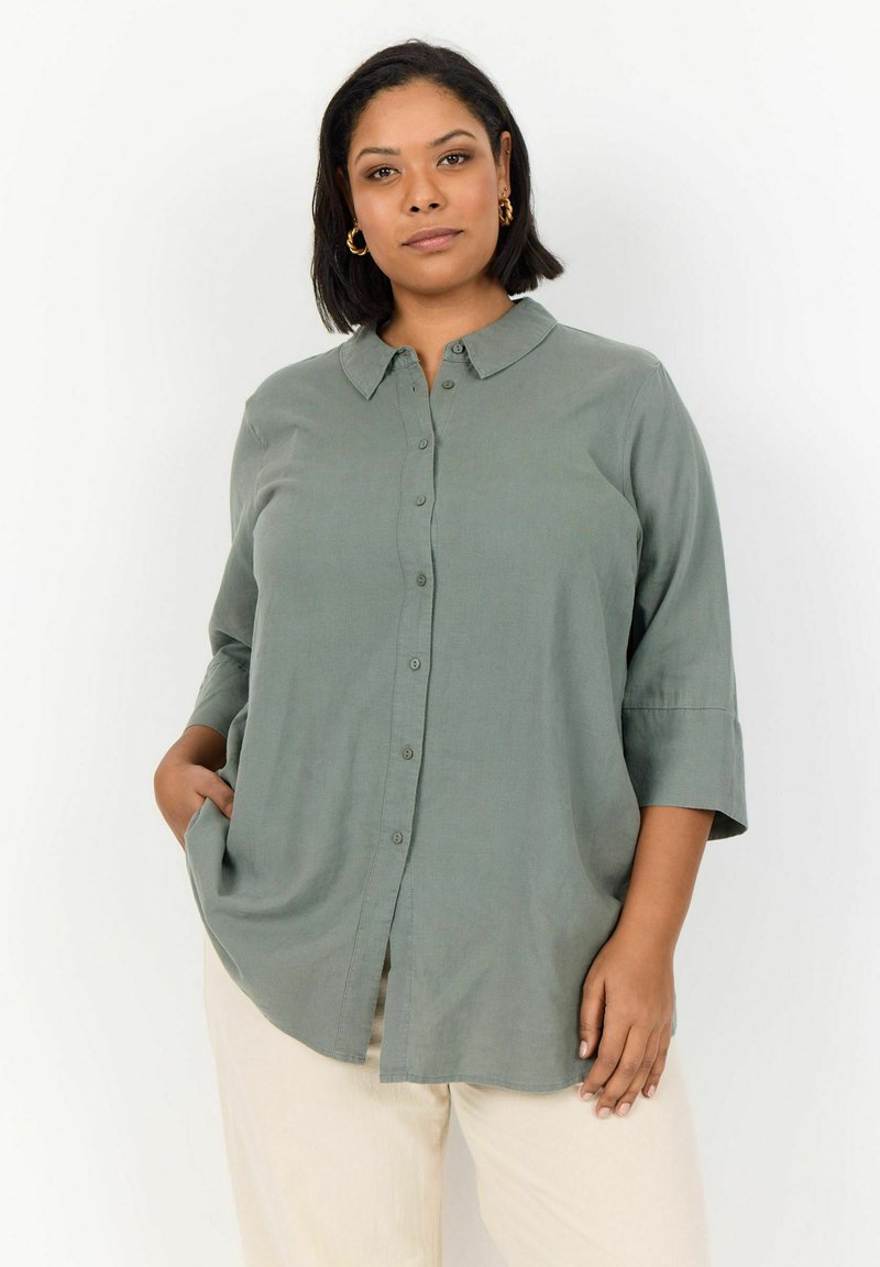 Light green button-up shirt with a collar, three-quarter sleeves, and side slits. Soft fabric with a smooth texture and relaxed fit.