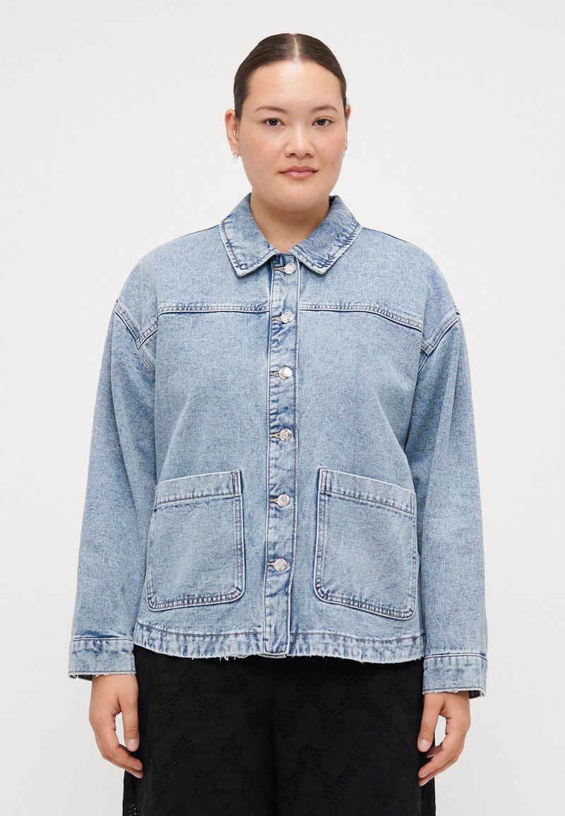 Lys blå denimjakke med spiss krage, frontlukking med knapper, to påsydde lommer og avslappet passform. Har kontraststing.