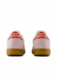 Rosa mockaskor med en gyllene gummisula. Röda detaljer pryder "New Balance"-logotypen på hälen, med en vit inredning.