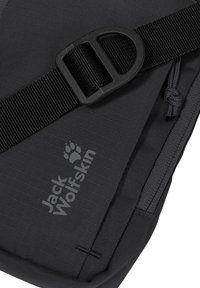 Gros plan d'un sac noir Jack Wolfskin avec une sangle ajustable, une boucle en plastique et une tirette de fermeture éclair ornée d'un cordon noué.