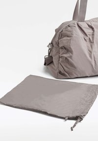 Harmaa kangasduffeli kerätyllä designilla ja sivulla metalliosat, vieressä tasainen, harmaa säilytyspussi. Molemmat esineet ovat sileäpintaisia.