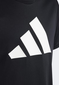 Camiseta negra de tejido suave, con un gran diseño de logo de tres rayas blancas en el frente, escote redondo y mangas cortas.