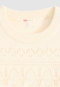 Pull en tricot blanc avec un col rond, présentant des motifs géométriques et un côtes texturées au niveau du col et de l'ourlet. Étiquette de taille visible.