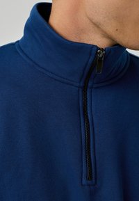 Sudadera con cremallera de color azul marino, con una textura suave, un cuello alto y detalles en cremallera negra que contrastan.