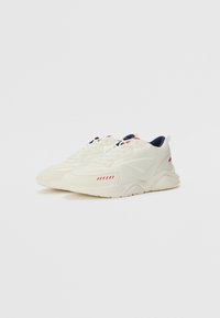 White sneakers with a textured surface, navy interior, red accent stripes on the side, and a chunky, sculpted sole design.