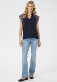 Marinblus med spetsärmar, V-ringning och mjukt tyg, kombinerad med ljusblå utsvängda jeans och svarta ballerina-skor.