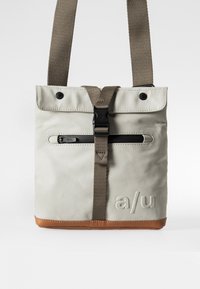 Borsa in tessuto grigio chiaro con fondo marrone, tracolla regolabile in tessuto, tasca frontale con cerniera e logo impressa nella parte inferiore.