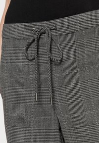 Grijze geruite broek van een gestructureerde stof, met een tailleband met trekkoord en zwarte hardwareaccenten.