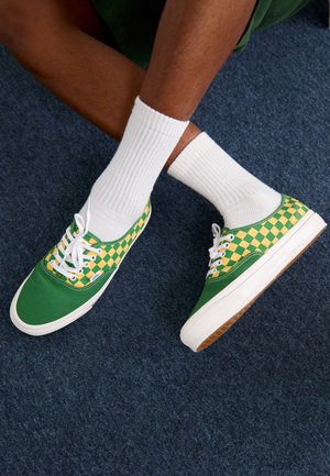 Grønne lærreds sneakers med et gult og grønt ternet mønster, hvide snørebånd og en hvid gummisål, båret med hvide ankelsokker.