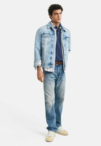 Ljusblå denimjacka över en marinblå polo, lager på lager med en vitrandig skjorta, ljusblå jeans och krämfärgade sneakers med en texturerad sula.