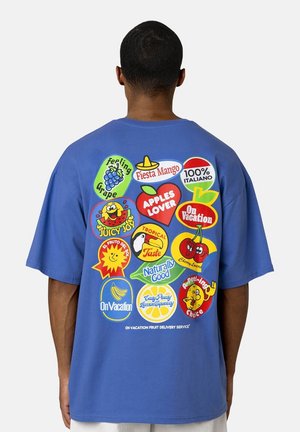 Blauwe katoenen t-shirt met kleurrijke fruit-thema grafische prints op de achterkant, waaronder appels, druiven, bananen en verschillende speelse slogans.