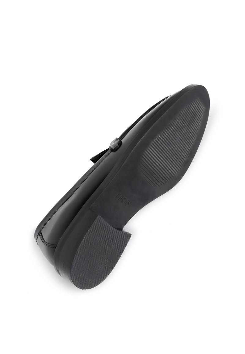 Chaussure en cuir noir avec une finition brillante, un petit talon et une semelle extérieure en caoutchouc texturé. Présente un petit bouton décoratif près de la sangle.