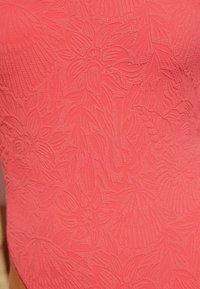 Enkelbitarssimdräkt i ljus korall med texturerade blom- och bladmönster, med upphöjda detaljer genom hela tygytan.