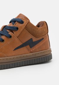 Baskets en cuir marron avec des lacets bleu foncé, des accents en suède et un design en éclaire navy. Semelle en caoutchouc texturée pour une bonne adhérence.