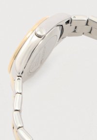 Montre en acier inoxydable avec une lunette dorée, bracelet argenté et doré lisse, et détail de couronne texturé. Logo gravé au dos.