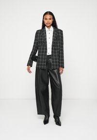 Karirani sako u crno-bijeloj boji, uparen s bijelom košuljom i crnim kožnim hlačama širokih nogavica, dopunjen šiljastim crnim štiklama.