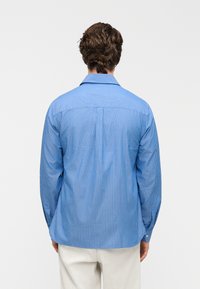 Μπλε ριγωτό μακρυμάνικο πουκάμισο με γιακά, με κάθετες λευκές ρίγες και μανσέτες με κουμπιά. Λείο ύφασμα, κανονική εφαρμογή με πίσω καβάλο.