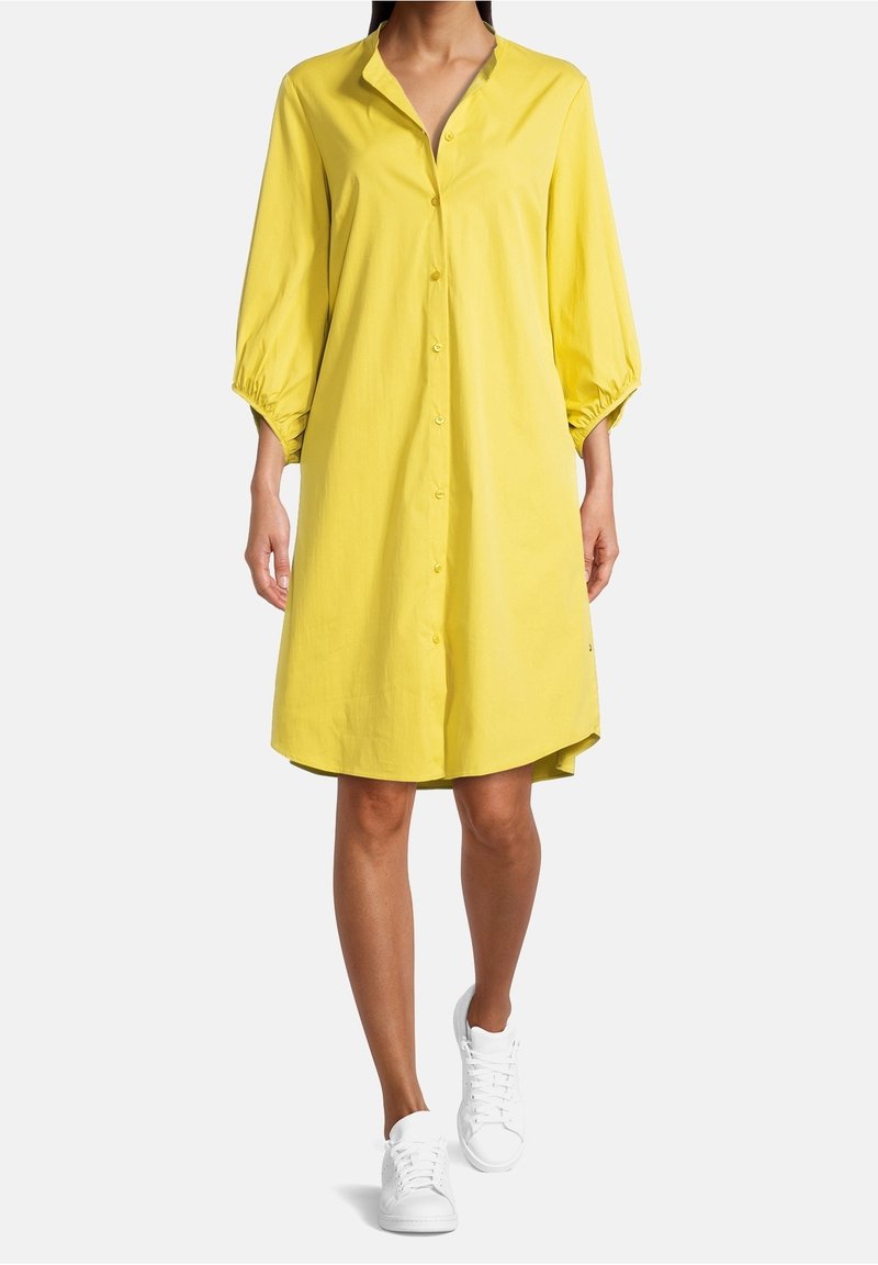 Robe chemise jaune avec col, manches ballon trois-quarts et coupe ample ; associée à des baskets blanches pour le contraste.