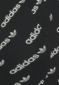 Černá tkanina s opakujícími se bílými nápisy "adidas" a vzory trojlístku. Hladká textura s přiléhavým střihem.