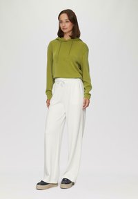 Sweatshirt à capuche verte, pantalon large blanc et baskets noires chunky. Tissu lisse avec une coupe décontractée ; les pantalons possèdent une taille à cordon.