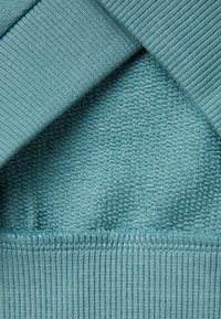 Capas de tela color aguamarina que presentan una suave textura tejida en la parte inferior y un acabado ribeteado y suave en la parte superior, con un borde sin costuras.