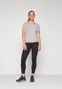 Camisola atlética cinzenta de mangas curtas combinada com leggings pretas e ténis pretos. Design simples e ajustado com pouca marcação.