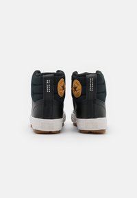 Sneakers neri alta con texture trapuntata, suola in gomma, intersuola bianca e logo circolare marrone sul tallone.