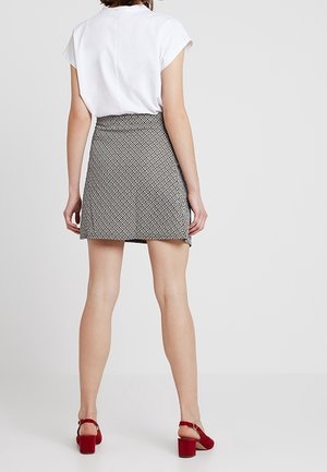 Mini-jupe à motif noir et blanc avec taille ajustée, portée avec des chaussures rouges à talons blocs et un haut blanc à manches courtes.