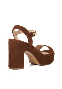 Sandales plates-formes en suede marron avec un talon large, bout ouvert et brides à la cheville embellies d'une boucle dorée. Doublure intérieure lisse.