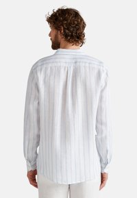 Camisa de manga larga a rayas en azul claro y blanco con un corte relajado. Confeccionada en tejido ligero, cuenta con puños abotonados y un detalle de pliegue en la parte trasera.