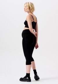Zwarte geribbelde crop top, gecombineerd met hoge zwarte capri leggings. Het model draagt zwarte plateau schoenen, heeft kort blond haar en staat in profiel.