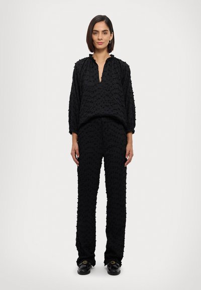 Black two-piece outfit featuring textured fabric, loose fit, long sleeves, and a V-neck top paired with straight-leg pants. Black footwear included.
