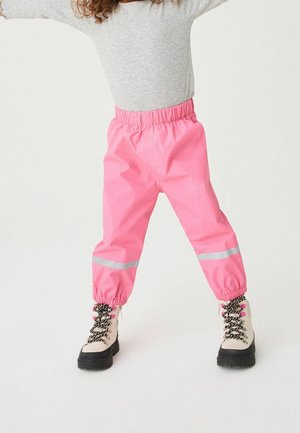 Pantalon imperméable rose avec bandes réfléchissantes, taille élastique et poignets froncés, associé à des bottes beiges avec des lacets noirs.