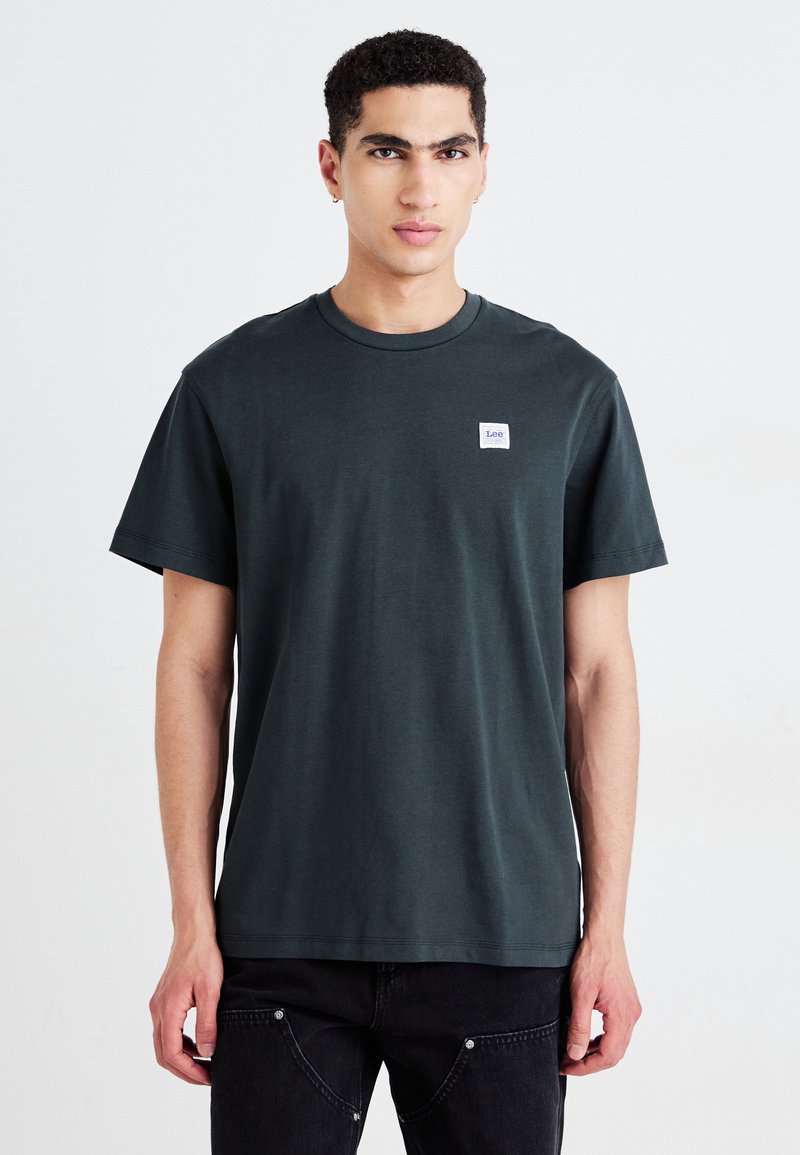 T-shirt in cotone verde scuro con maniche corte, collo rotondo e un piccolo etichetta bianca sul petto. Presenta una vestibilità rilassata.