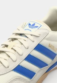 Canvas sneakers met blauwe strepen, beige accenten en gestructureerde stof. Beschikt over een blauwe logopatch en vetersluiting.