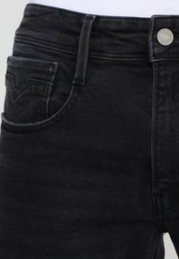 Svarta denimjeans med en figurnära design, en framficka med sömdetaljer och ett synligt metalldesignat knäpplås i midjan.