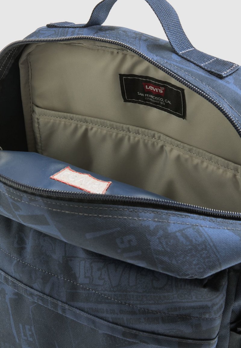 Mochila azul con un exterior texturizado, cierre de cremallera, interior en gris claro y una etiqueta que indica la marca "Levi's" en el interior.