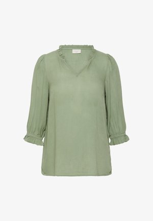 Blouse vert clair avec un col en V et un col à volants. Elle présente des manches trois-quarts avec des poignets froncés et un tissu texturé.