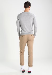 Pull gris et pantalon kaki. Le pull a un ourlet côtelé ; le pantalon est ajusté avec des poches arrière. Chaussures blanches avec des accents rouges.