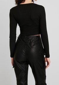 Schwarzes, geripptes, langärmeliges Cropped-Top, kombiniert mit hochgeschnittenen schwarzen, faux-ledernen Hosen mit Seitentaschen und nahtlosem Rücken.