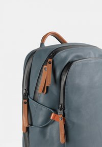 Zaino blu in pelle con una forma strutturata, caratterizzato da dettagli in pelle marrone e cerniere nere. Include diversi scomparti con cerniera e cinturini.