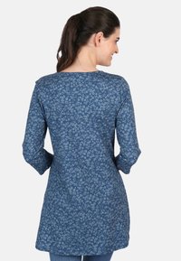 Blaue Blumentunika mit langen Ärmeln, weichem Stoff, rundem Halsausschnitt und einem floralen Muster aus kleinen Blumen. Taillierter Schnitt in der Taille.