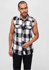 Fekete-fehér kockás, ujjatlan flaneling két mellzsebbel és gombos elülső résszel, sötét nadrággal párosítva.