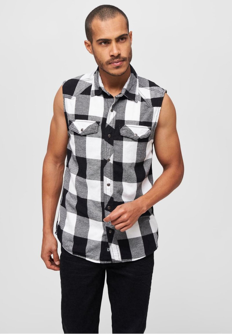 Svart och vit rutmönstrad, ärmlös flanellskjorta med två bröstfickor och knäppning framtill, kombinerad med mörka byxor.