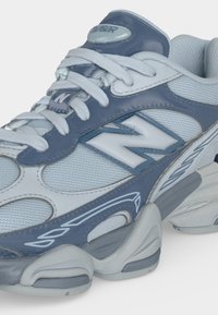 Крупен план на бяла и сива спортна обувка New Balance с мрежеста материя, синтетични наслоявания и дебела подплатена подметка.
